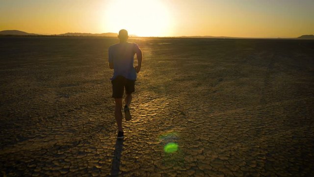 Athletic man working out with battle ropes on a dry lake at sunset