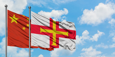 China and Guernsey flag waving in the wind against white cloudy blue sky together. Diplomacy concept, international relations.