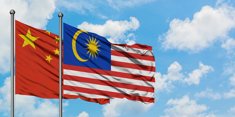 China and Malaysia flag waving in the wind against white cloudy blue sky together. Diplomacy concept, international relations.