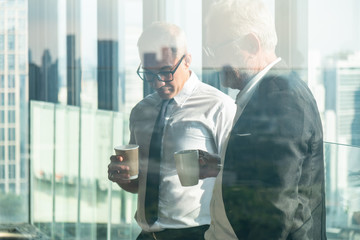 business background of two businessman standing together with hands holding a cup of coffee during having business talking, view through office window
