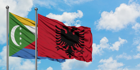 Comoros and Albania flag waving in the wind against white cloudy blue sky together. Diplomacy...