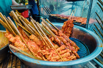 Chicken strips put in bamboo sticks and dipped in special sauces in basin preparation to grill for sale in local market