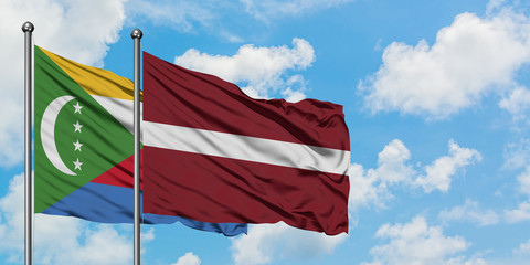 Comoros and Latvia flag waving in the wind against white cloudy blue sky together. Diplomacy...