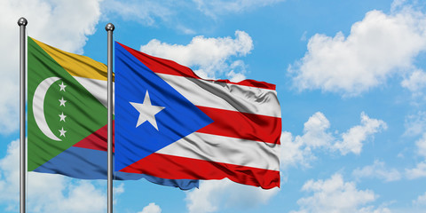 Comoros and Puerto Rico flag waving in the wind against white cloudy blue sky together. Diplomacy...