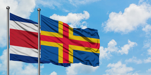 Costa Rica and Aland Islands flag waving in the wind against white cloudy blue sky together. Diplomacy concept, international relations.