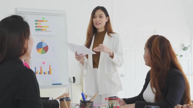 Beautiful young asian businesswoman  presents business profits to colleagues at meeting, explaining business turn over on flipchart to coworkers in office.