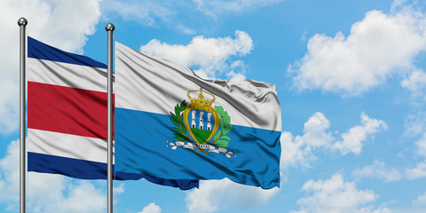 Costa Rica and San Marino flag waving in the wind against white cloudy blue sky together. Diplomacy...