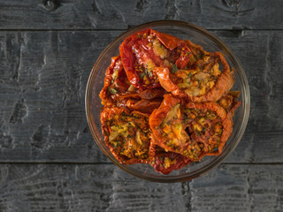 Top view of a glass bowl of sun-dried tomatoes on a black table. Vegetarian food.