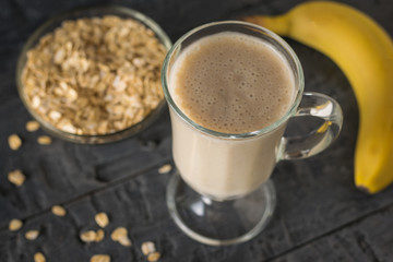 Freshly made banana smoothie, banana and bowl of oatmeal on the table. Vegetarian smoothie.