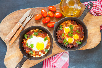 Pan of fried eggs and cherry-tomatoes with bread on dark table surface, top view, copy space, selective focus
