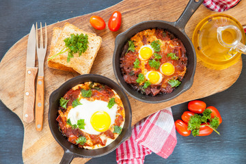 Pan of fried eggs and cherry-tomatoes with bread on dark table surface, top view, copy space, selective focus