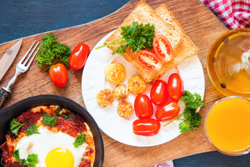 Pan of fried eggs and cherry-tomatoes with bread on dark table surface, top view, copy space, selective focus