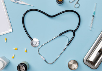 Stethoscope in shape of heart with medical documents, thermometer, syringe and pills on blue table background, Good health from Doctor concept, Top view with copy space, Isolated on blue