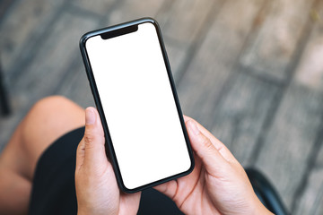 Top view mockup image of a woman holding a black mobile phone with blank white desktop screen