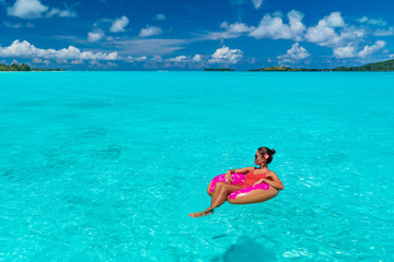 Vacation beach woman relaxing on inflatable donut float swimming in paradisiac turquoise ocean. Summer travel sun tan lifestyle for winter holidays getaway vacation. Caribbean tropical luxury resort.