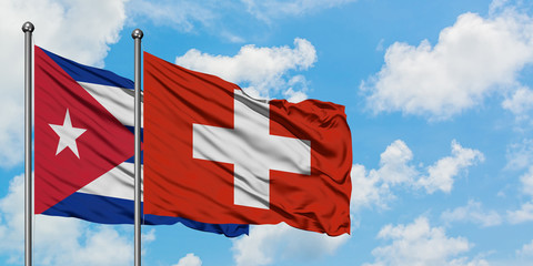 Cuba and Switzerland flag waving in the wind against white cloudy blue sky together. Diplomacy...