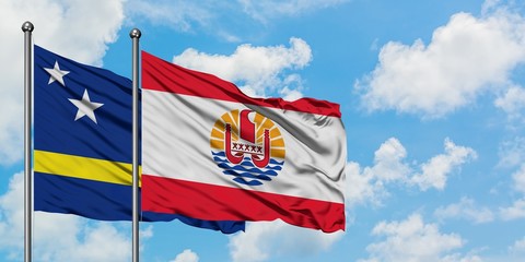 Curacao and French Polynesia flag waving in the wind against white cloudy blue sky together. Diplomacy concept, international relations.
