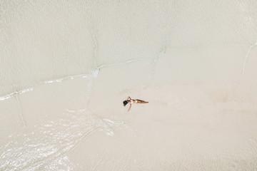 Aerial drone shot of woman lying in water on white sand beach and enjoying vacations. Tropical travel concept.