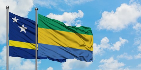 Curacao and Gabon flag waving in the wind against white cloudy blue sky together. Diplomacy concept, international relations.