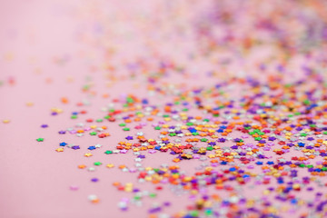 The selective focus photo of the colored confetti in the form of stars. Abstract textured background toned pink color