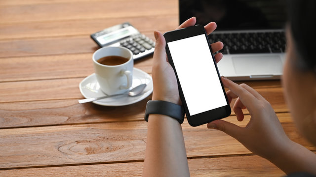 Cropped shot top view of businesswoman hands using smartphone mockup on office desk. Blank screen mobile phone for graphic display montage.