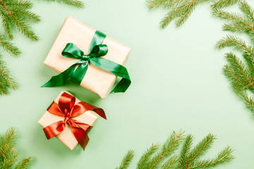 Two Christmas gift boxes with green and red ribbon on light green background with branch of fir tree
