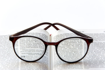 Open holy bible in bahasa Indonesia (Yeremia 29:11) on white background with glasses close up