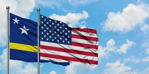 Curacao and United States flag waving in the wind against white cloudy blue sky together. Diplomacy concept, international relations.