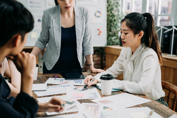 group of web designers developing new website layout in modern office. confident pregnant woman manager standing at table in board room listening to employee asking question. creative team workers