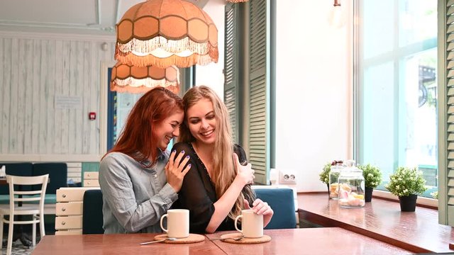 Two same-sex lovers sit in a cafe and drink coffee. Attractive gay women talking and laughing. Lesibians do not hide their feelings in a coffee shop and show affection for each other