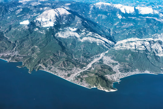 Mountain ridges and city aerial panoramic view in Russia. Sea meets the land with urban settelment at the foot of hills with white peaks. Geographic location and travel destination. Mountains crests