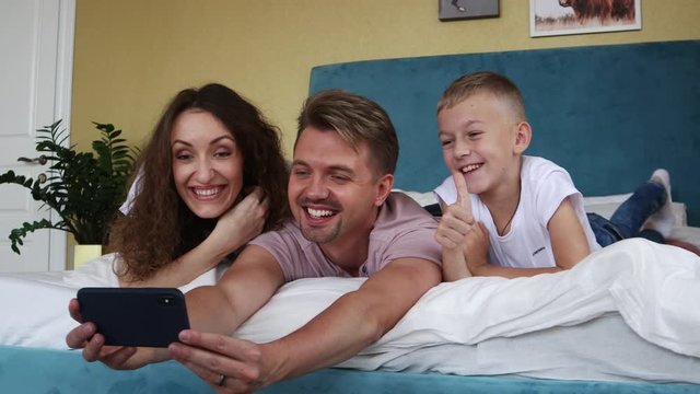 Cheerful family of a young mother father and son making a video call while lying on the bed.