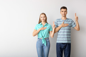 Fototapeta premium Young man and woman taking oath with hand on chest and raised fingers, pledging loyalty or making promise, studio portrait isolated on light background with copy space