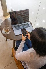 Woman using cellphone while sitting at coffee table with laptop