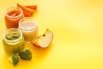 Baby food. Colorful puree in glass jars near vegetables and fruits on yellow background copy space