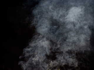 Puffs of white smoke in blurred dynamics on a dark background. Studio photography