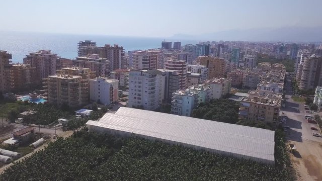Aerial view of the large farm land and warehouse near the modern buildings and seashore resort in summer sunny day against blue sky. Clip. Beautiful view from above