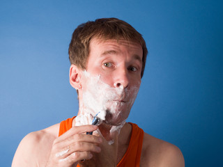 Close-up. The guy enthusiastically shaves his chin. Studio photography on a blue background