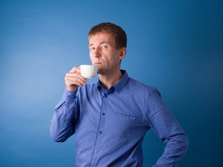 Guy in a blue shirt on a blue background drinks coffee. Studio photography on a blue background