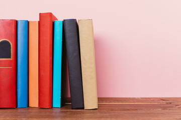 A simple composition of many hardback books, raw books on a wooden table and a pale pink background
