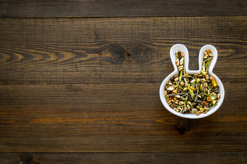 Pet food for rabbits in rabbit-shaped bowl on dar wooden background top view copy space