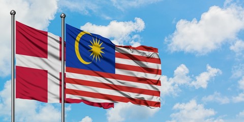 Denmark and Malaysia flag waving in the wind against white cloudy blue sky together. Diplomacy concept, international relations.