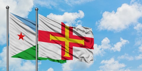 Djibouti and Guernsey flag waving in the wind against white cloudy blue sky together. Diplomacy...