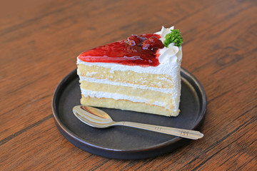 Strawberry cake in metal tray with spoon on wooden table.