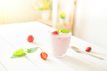 Yogurt with strawberry in glass on wooden white table in interior