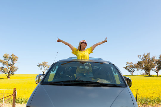 Happy woman standing out the sunroof of her 4wd car by canola field