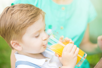 Cute kid boy drinking a glass of fresh orange juice