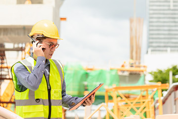 Image outside the industrial construction engineers in yellow protective helmet discuss new project while walkie talkie and happy smile on the open building site near the crane.
