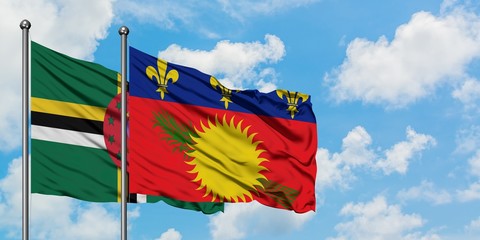 Dominica and Guadeloupe flag waving in the wind against white cloudy blue sky together. Diplomacy...