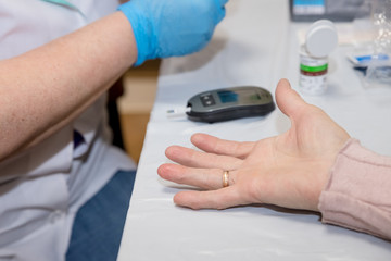 Doctor testing a patients glucose level after pricking his finger to draw a drop of blood and then using a digital glucometer.Senior diabetic woman is having a check up at home from a district nurse